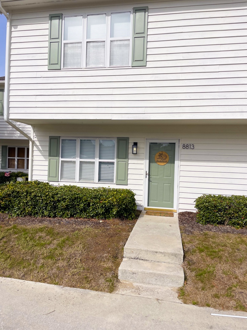 Clean white siding with sage green shutters and door creates welcoming curb appeal at this well-maintained property entrance.