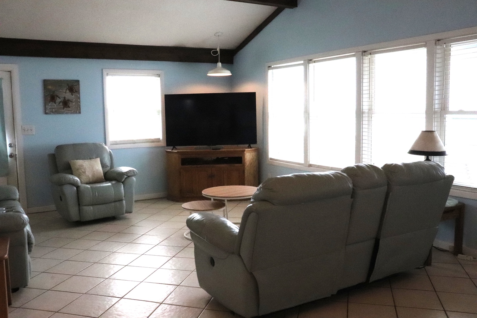 Relax in your spacious living room featuring plush recliners, a large flat-screen TV, and abundant natural light streaming through multiple windows—perfect for unwinding after exploring.