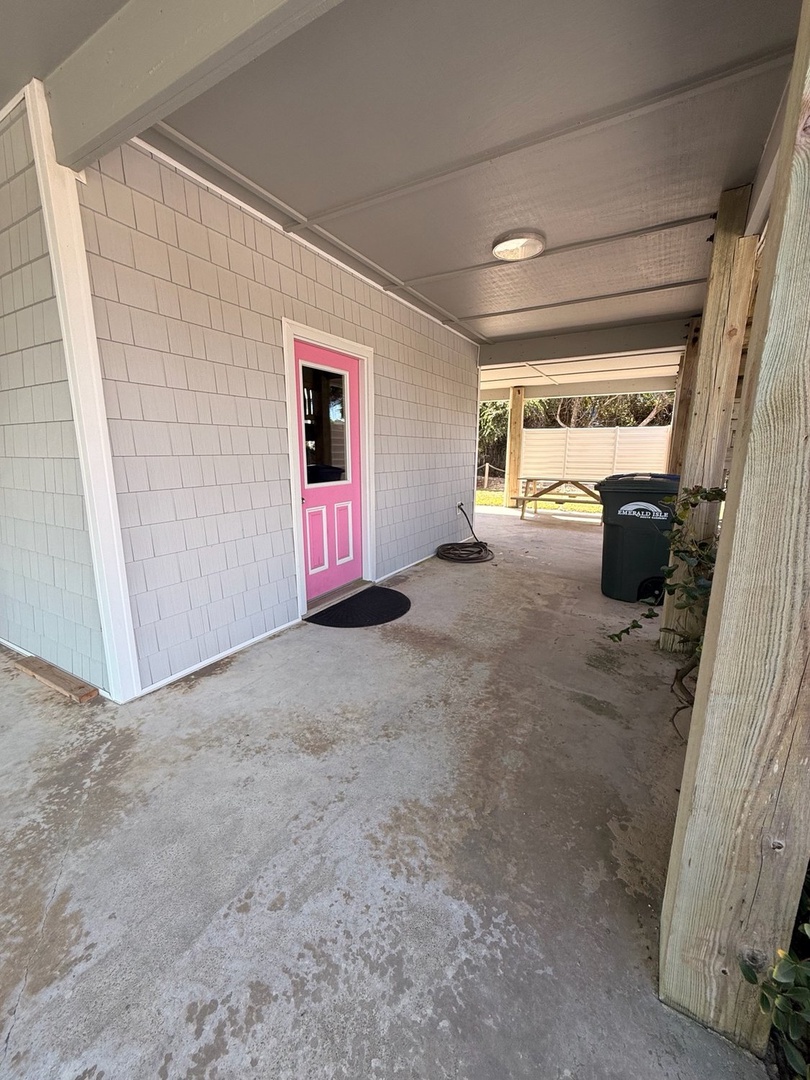 A covered carport provides convenient parking and easy access through the cheerful pink door to your vacation home.