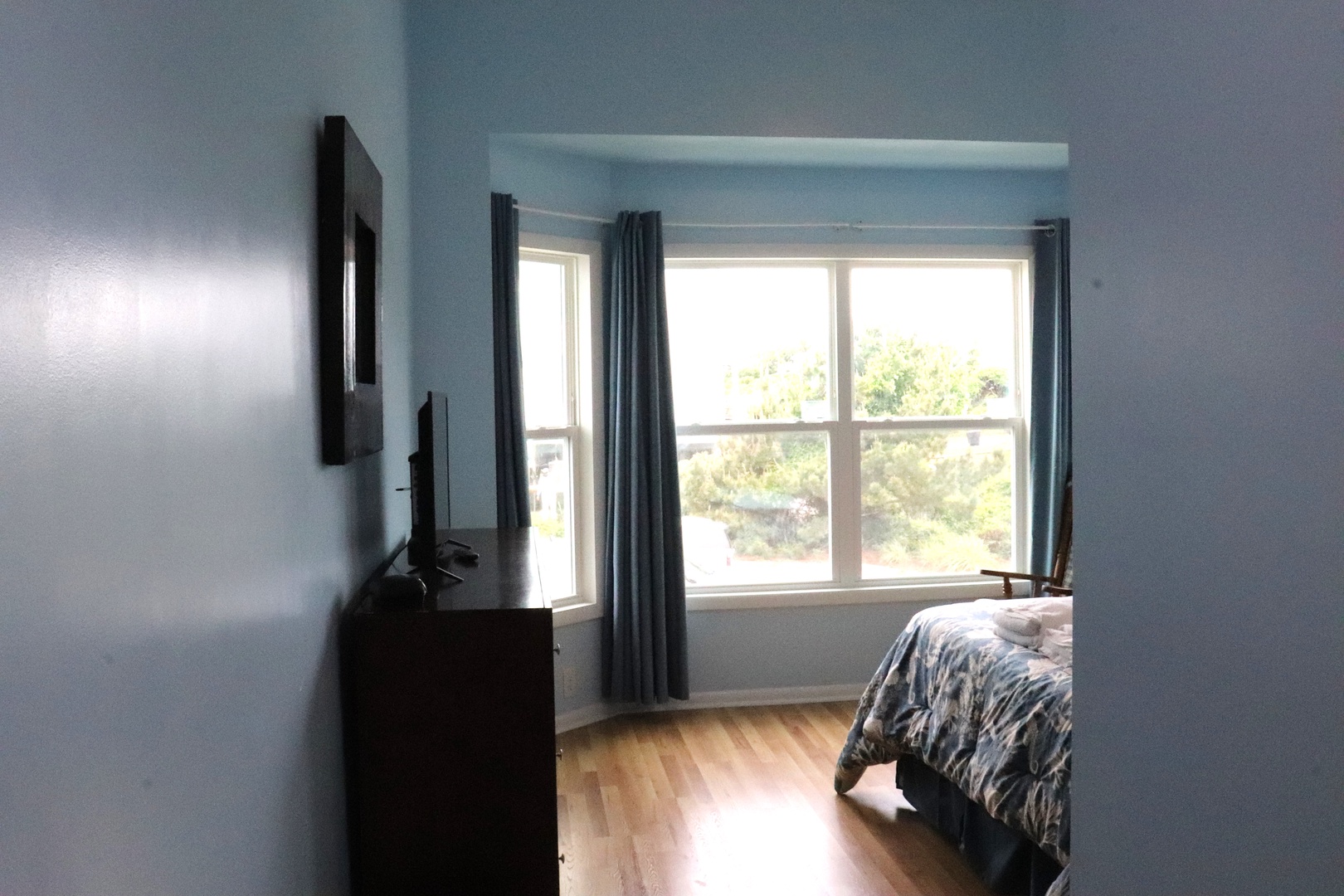 Your bedroom offers peaceful natural light through large windows, with warm hardwood floors and a mounted TV for your entertainment and relaxation.