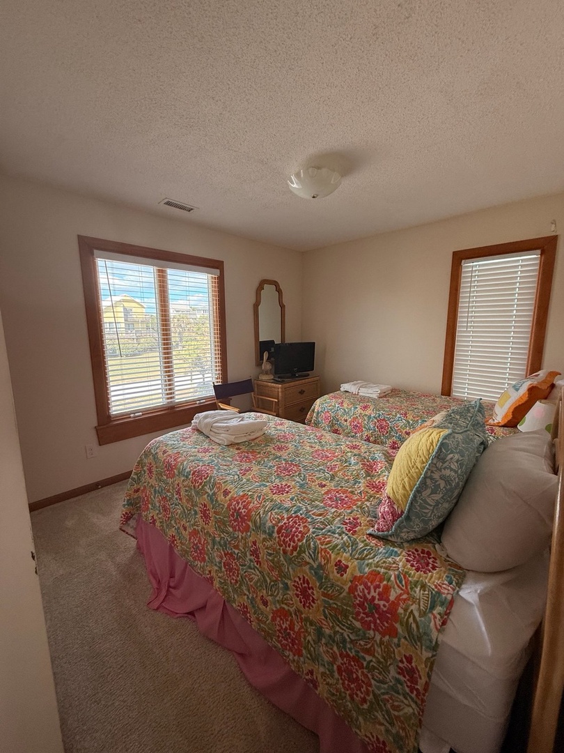Settle into your cheerful bedroom where colorful quilts and plush pillows invite restful nights, while bright windows frame distant blue skies and peaceful surroundings.