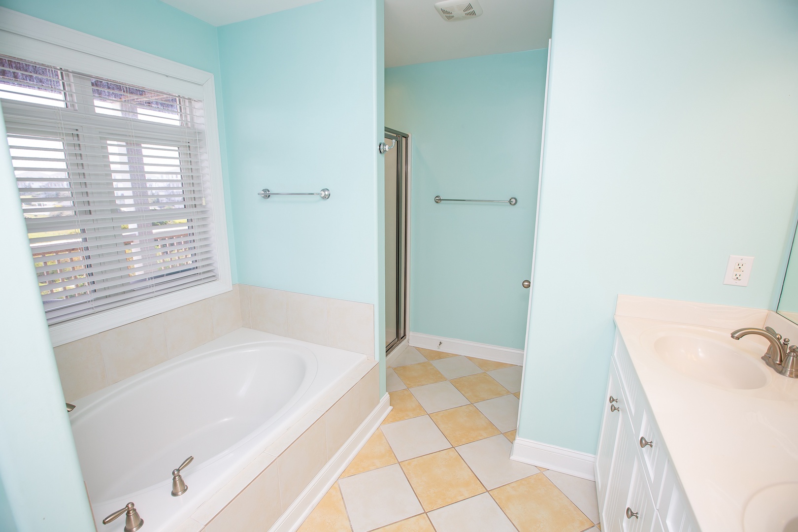 Unwind in your spacious bathroom with soothing mint walls, deep soaking tub, and bright natural light streaming through blinds.
