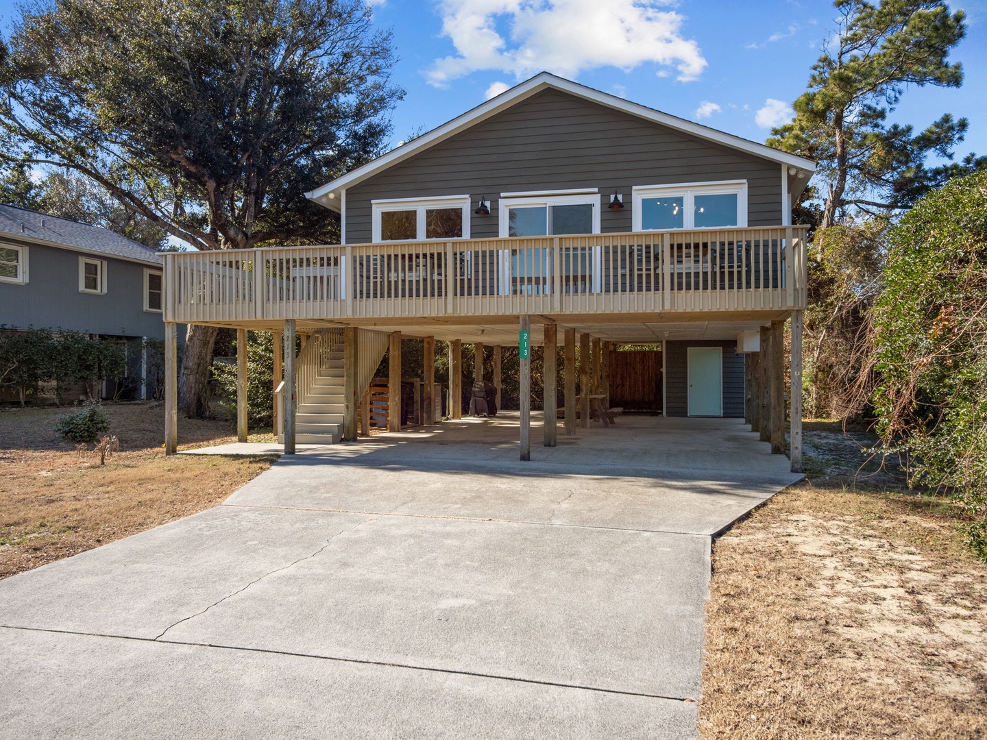 Elevated beach cottage with spacious deck surrounded by mature trees and convenient parking.