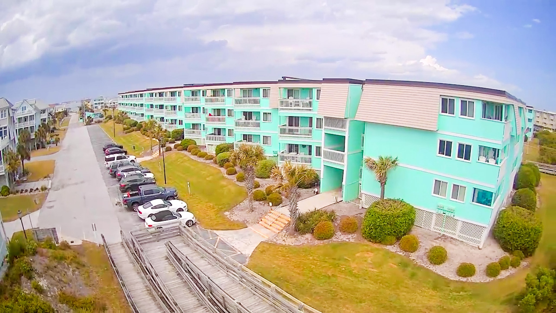 Beachfront property featuring colorful turquoise buildings with convenient parking and tropical landscaping in a peaceful coastal setting.