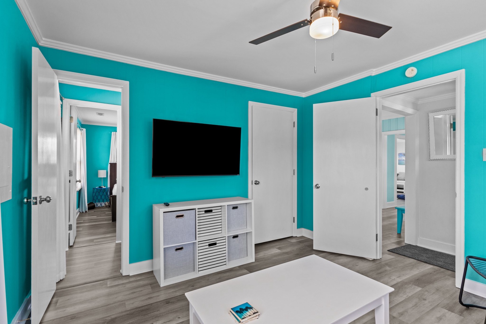 Relax in your bright living space with turquoise walls, modern entertainment center, and ceiling fan keeping you cool.