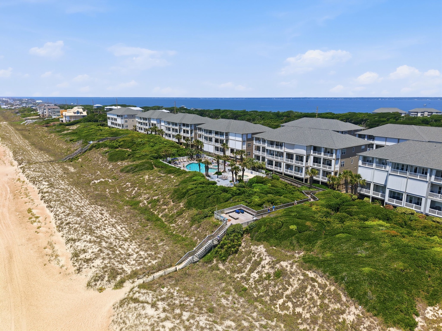 This beachfront property features direct dune access to the sandy shore, swimming pool facilities, and coastal views. Located in a natural coastal setting with palm trees and ocean views.