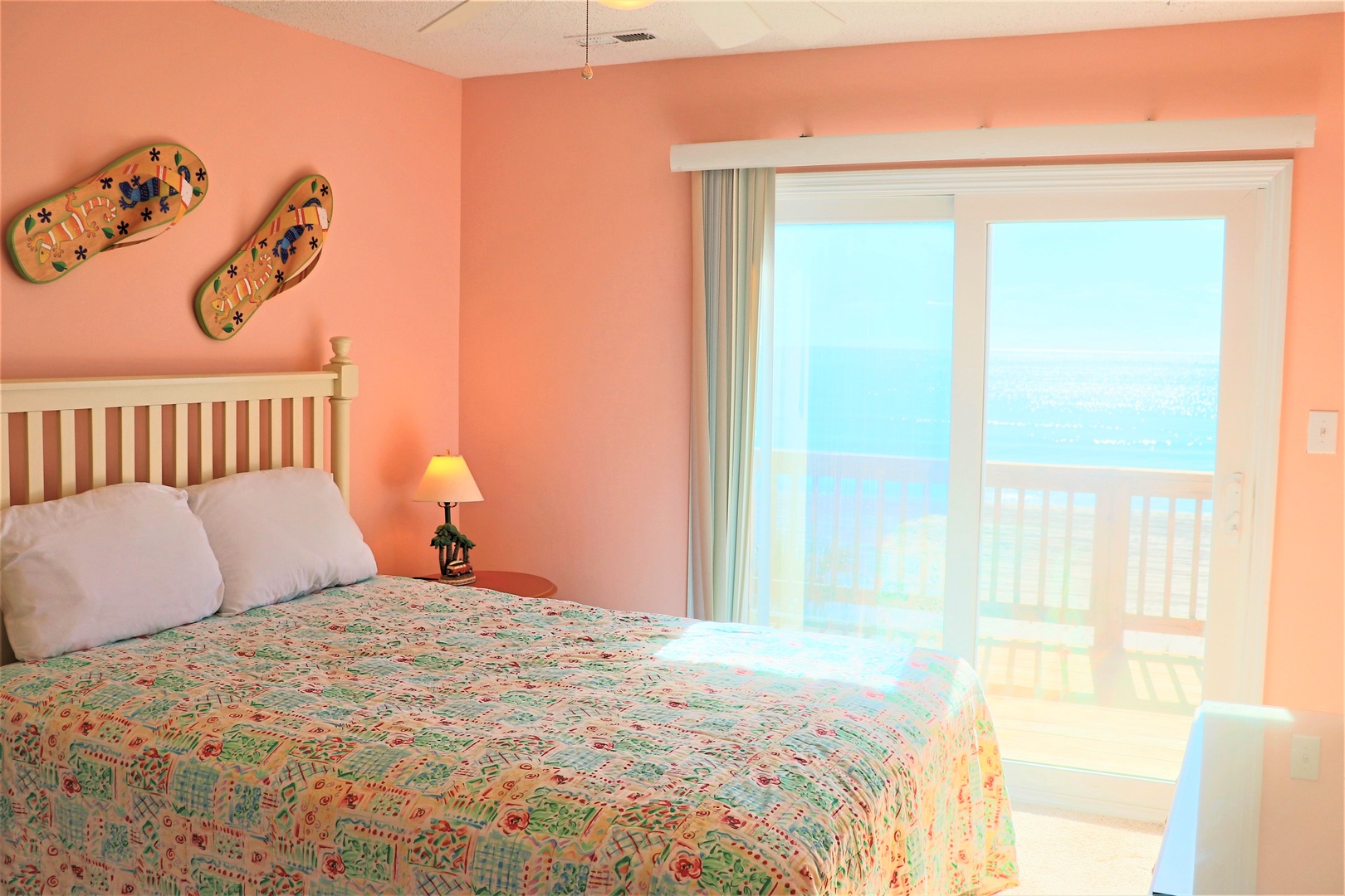 Wake up to stunning ocean views from your cozy bedroom, where cheerful coral walls and tropical flip-flop art create the perfect beach getaway atmosphere.