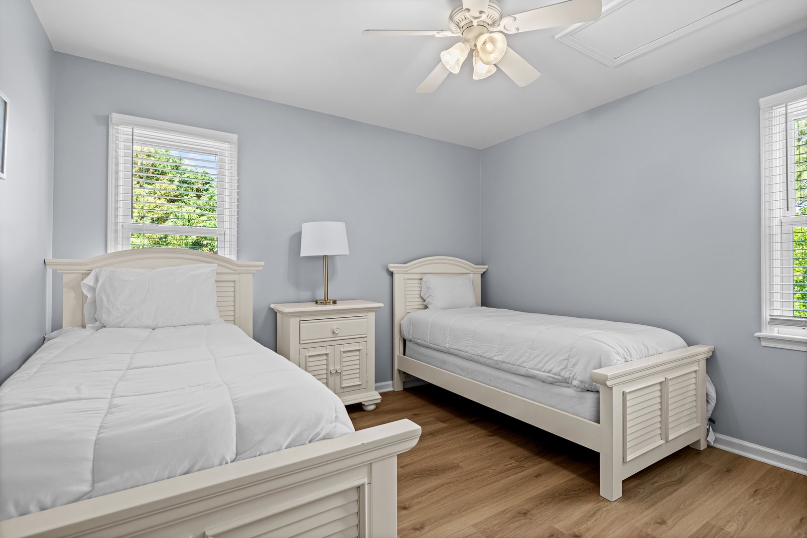 Sleep peacefully in your bright twin bedroom with classic white furnishings, hardwood floors, and gentle ceiling fan breeze.