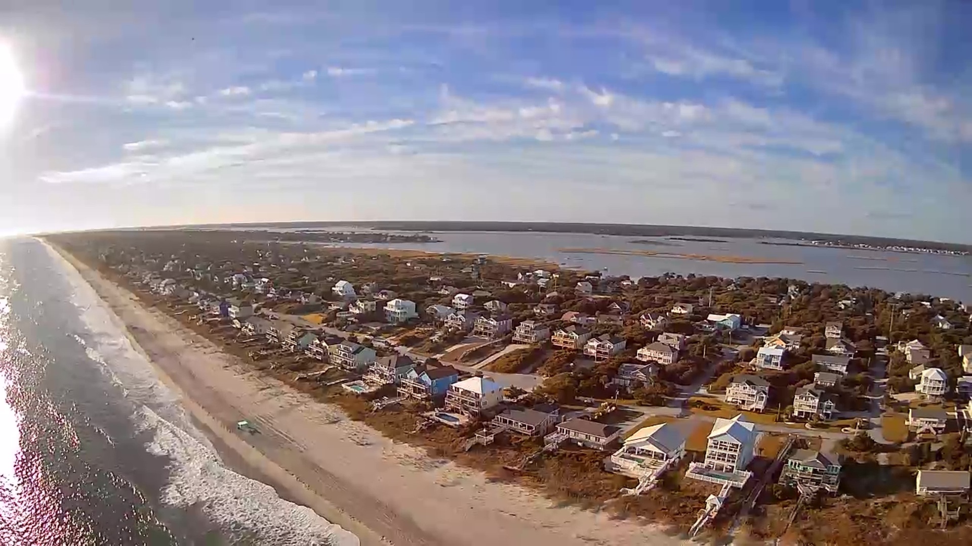 Aerial view of coastal community with beach homes nestled between pristine shoreline and calm bay waters.