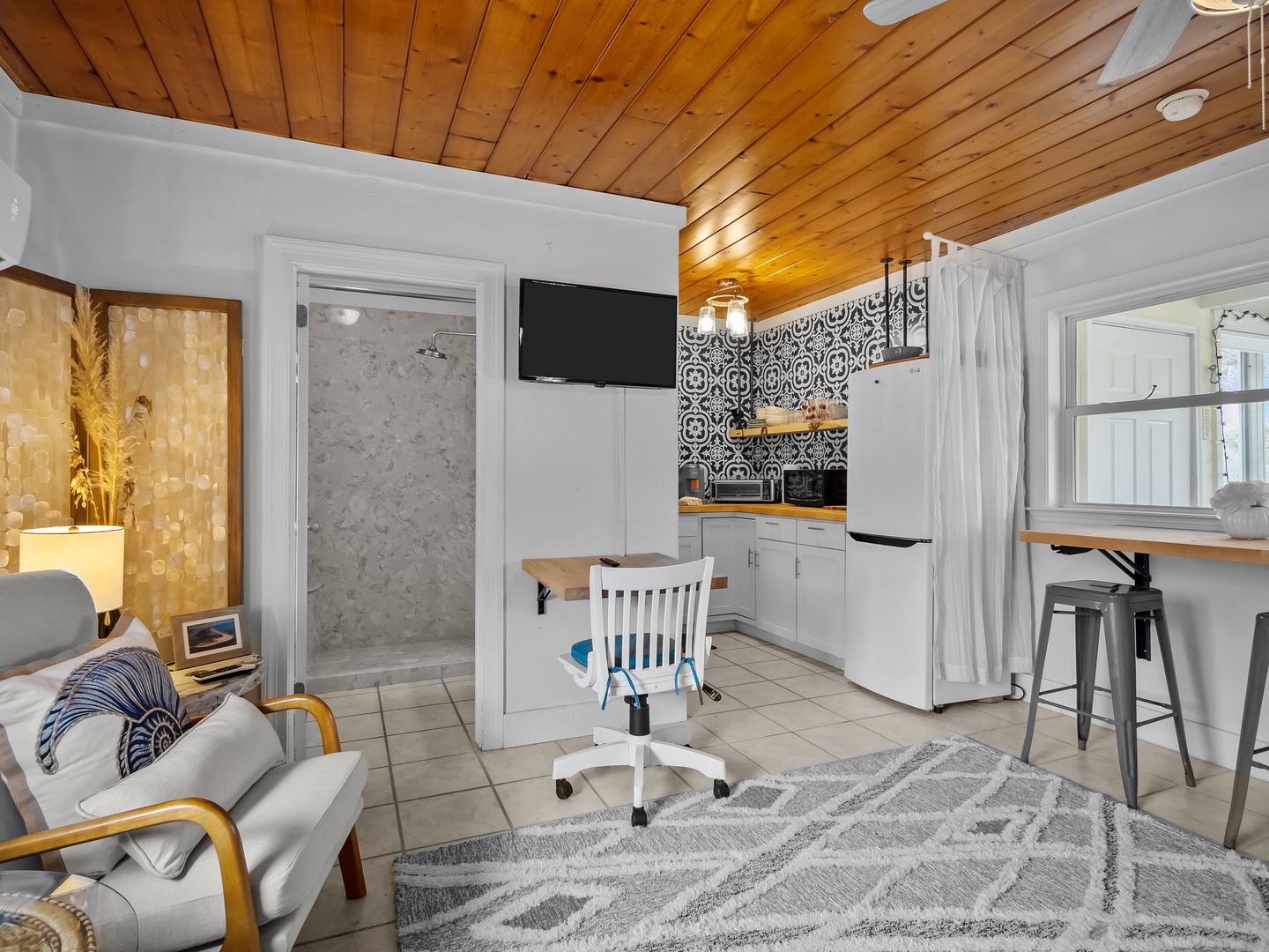 Relax in your stylish studio featuring warm wood ceilings, a fully equipped kitchen with patterned backsplash, and thoughtful details for remote work.