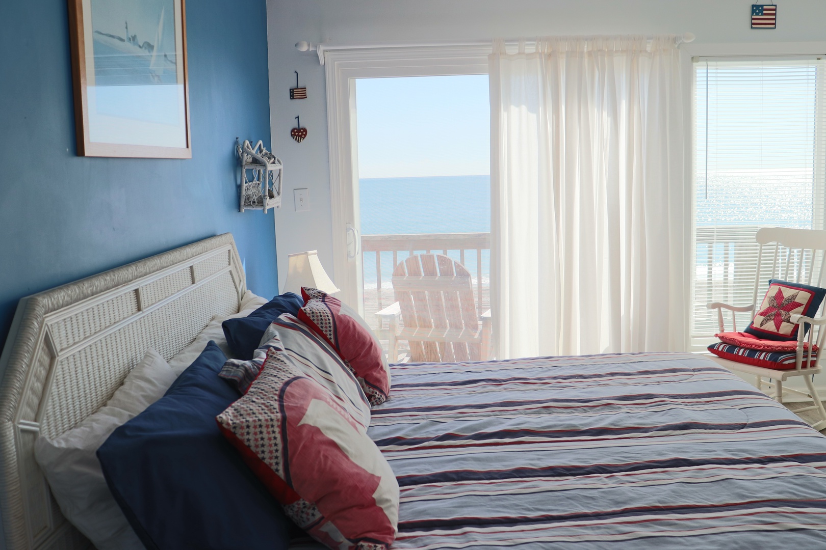 Wake to stunning ocean views from your cozy bed, with soft morning light streaming through white curtains and a private balcony just steps away.