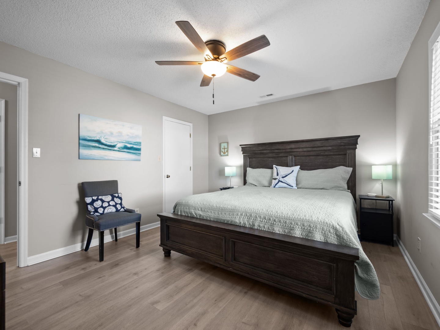 Relax in your serene bedroom with coastal-inspired decor, comfortable seating, and gentle ceiling fan breeze for perfect sleep.