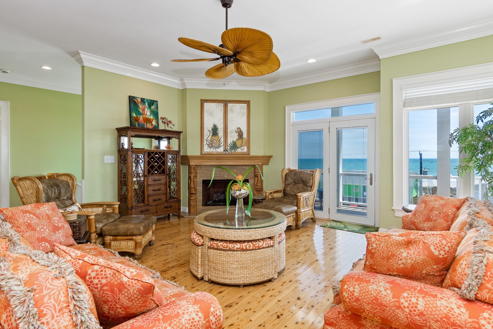 Your tropical-inspired living room features vibrant coral seating, wicker accents, and stunning ocean views through French doors to create a coastal paradise.