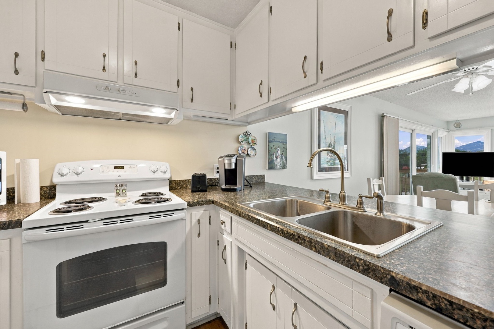 Step into your fully equipped kitchen, where granite counters, white cabinetry, and modern appliances make preparing meals effortless. Natural light streams through the window, framing stunning mountain vistas beyond.