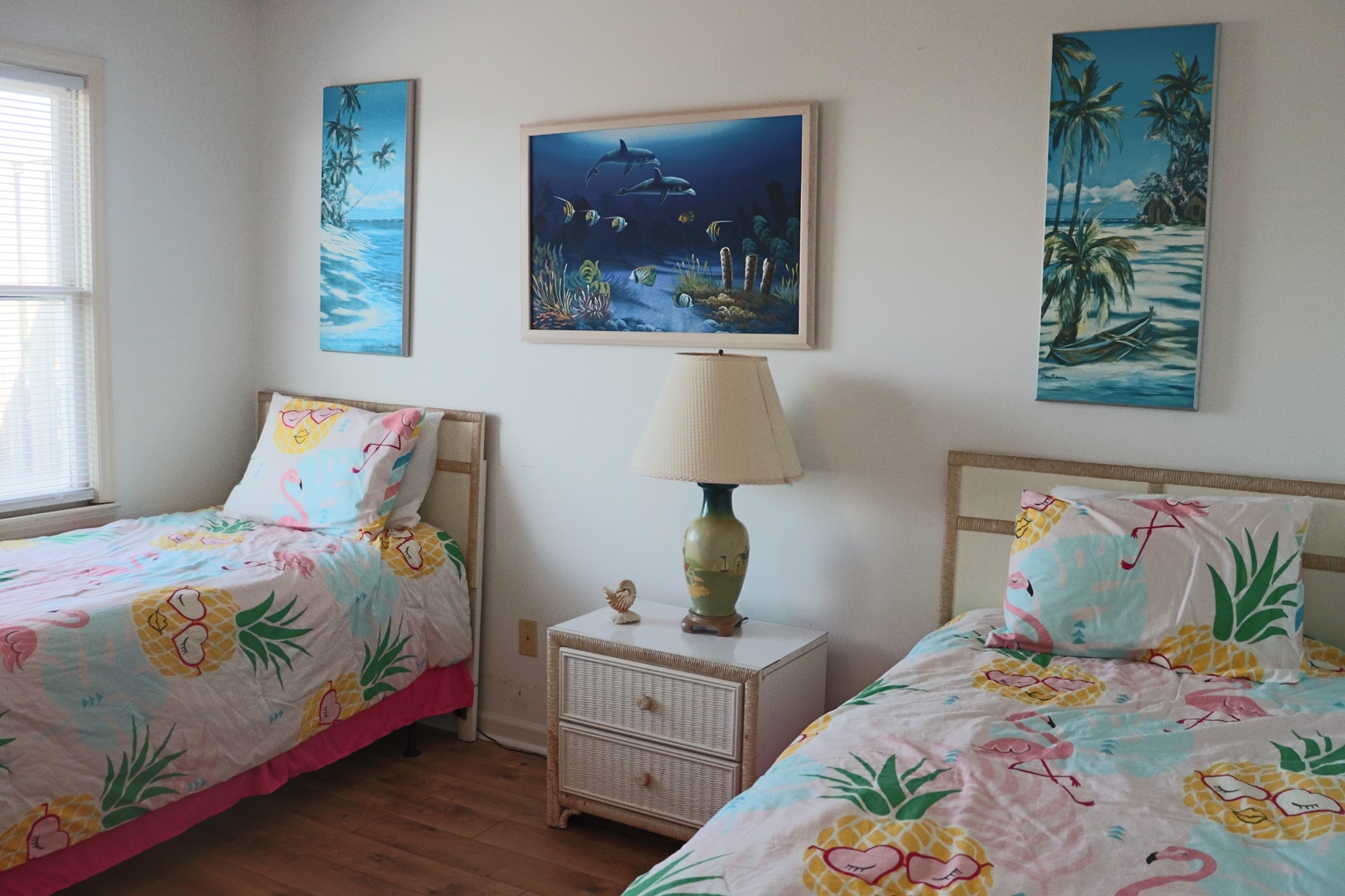 Your tropical-themed bedroom features twin beds with cheerful pineapple and flamingo bedding, ocean artwork creating a playful island atmosphere.