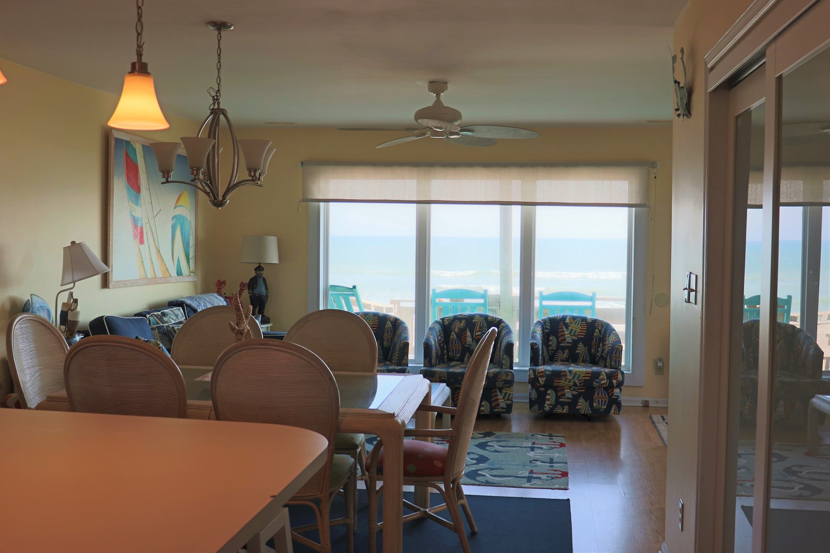 Your oceanfront living space flows seamlessly from dining to relaxation, with endless sea views through floor-to-ceiling windows and turquoise beach chairs awaiting you outside.