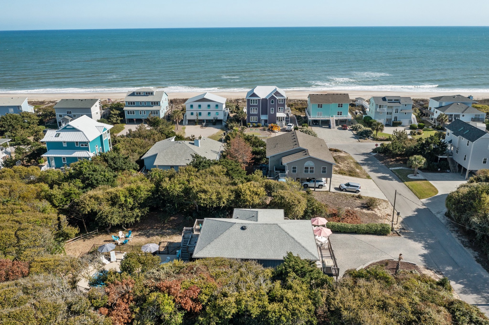 Aerial view of coastal neighborhood with beach houses nestled among native vegetation, just steps from pristine sandy shores and ocean waves.