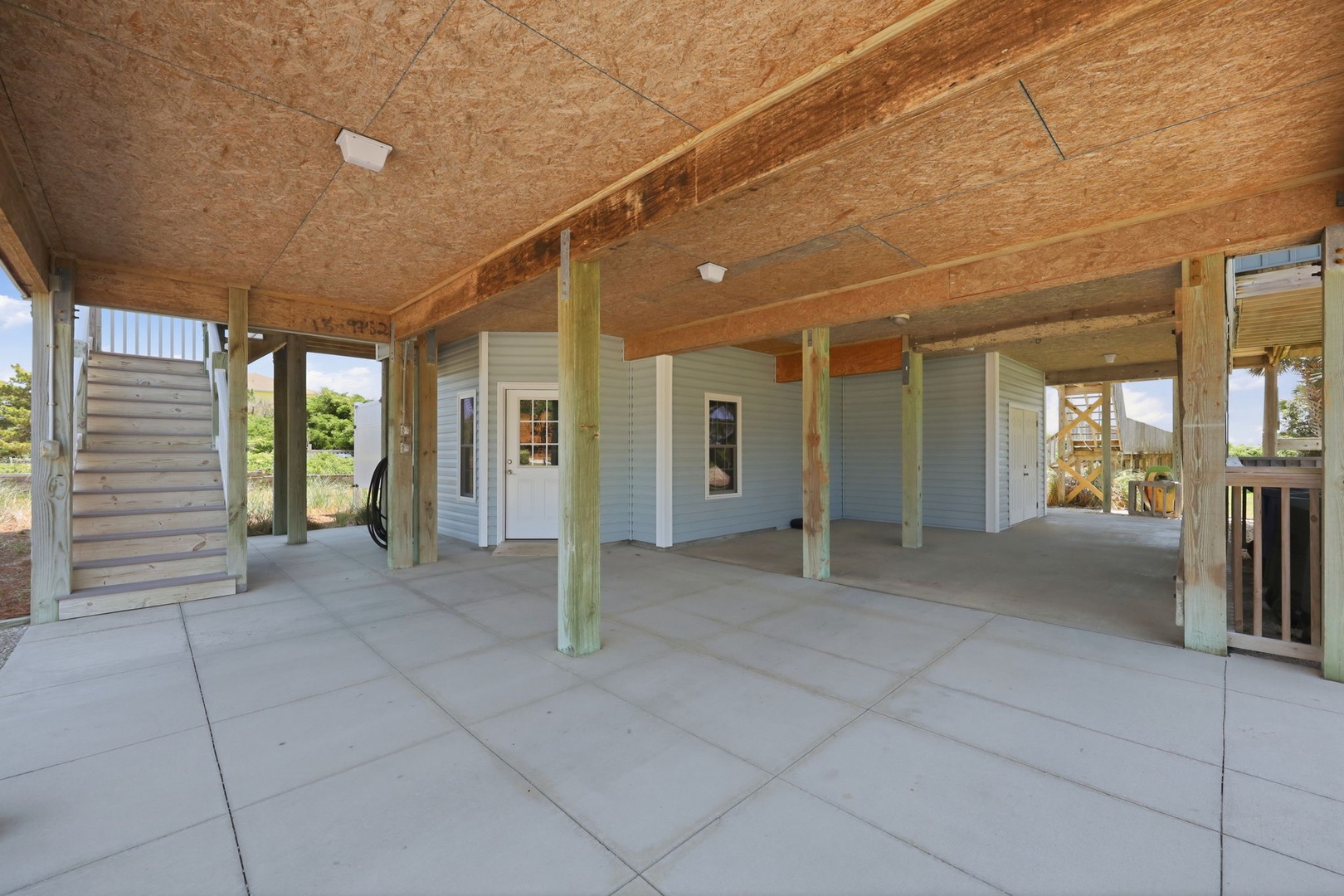 Protected covered parking area beneath the property with sturdy wooden beams and open access to the waterfront outdoors, offering secure vehicle and storage space.