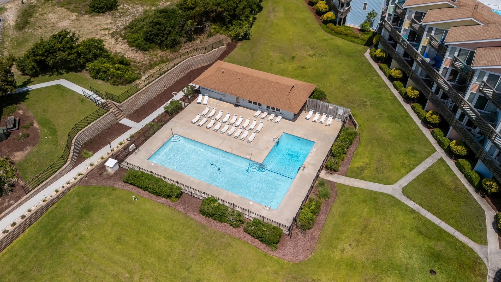 Aerial view of resort swimming pool complex with spacious deck area surrounded by landscaped grounds and residential buildings.