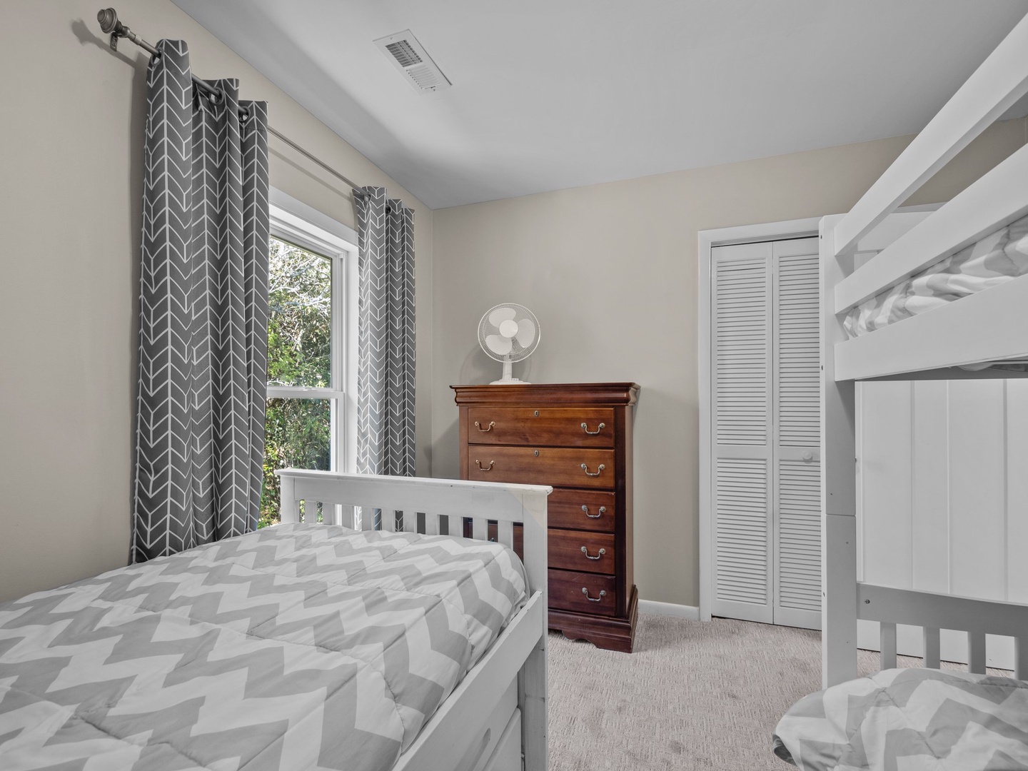 Sleep soundly in this cozy bedroom featuring comfortable beds, ample storage, and soft natural light filtering through patterned curtains.