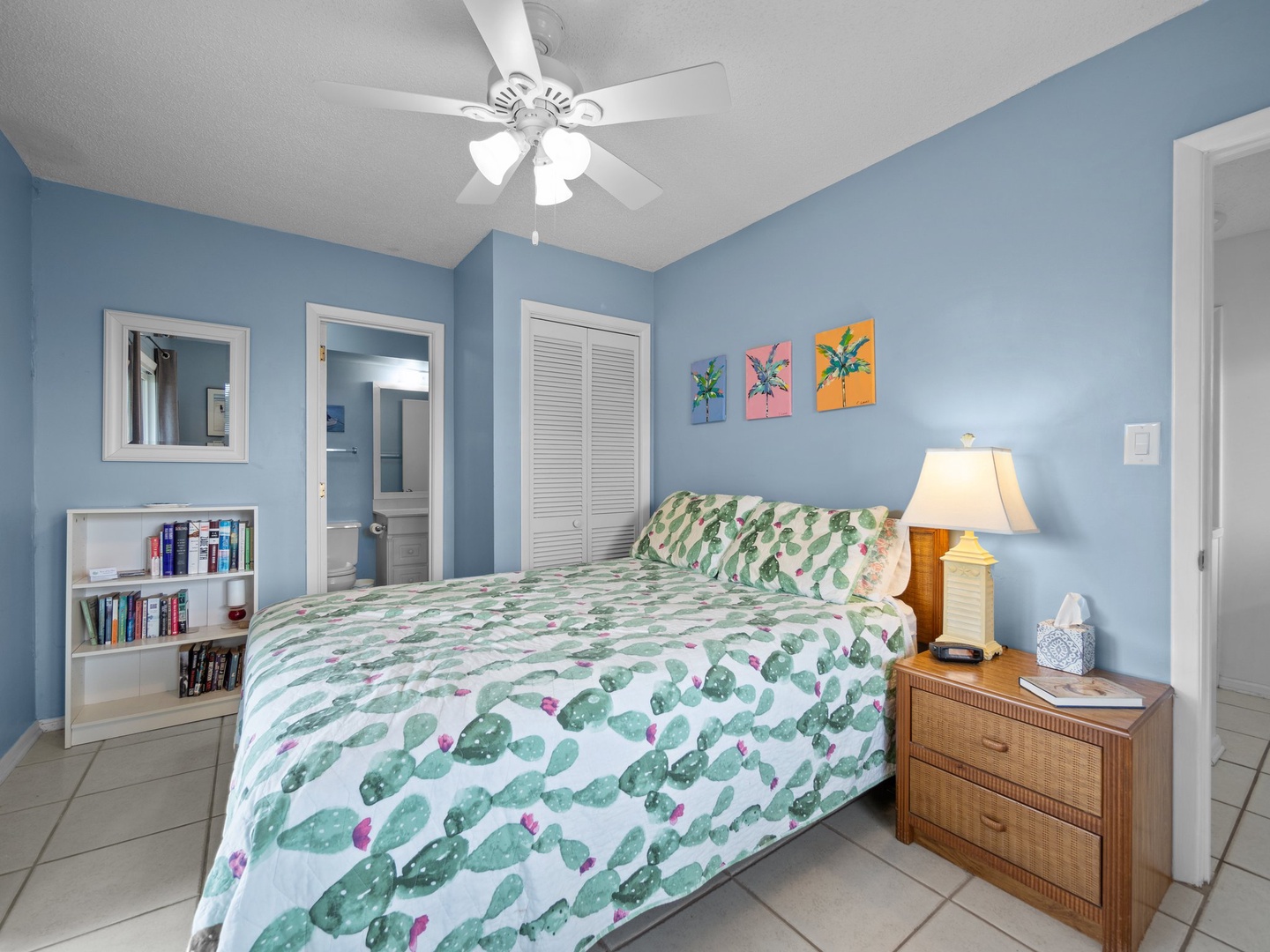 Unwind in your bright bedroom with coastal blue walls, tropical bedding, and a ceiling fan for comfort.