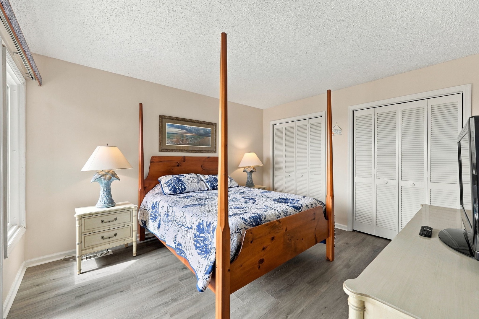 Settle into your elegant four-poster bed beneath soft linens, where coastal charm meets refined comfort. The bedroom's serene palette and natural light create a perfect retreat after a day exploring the area.