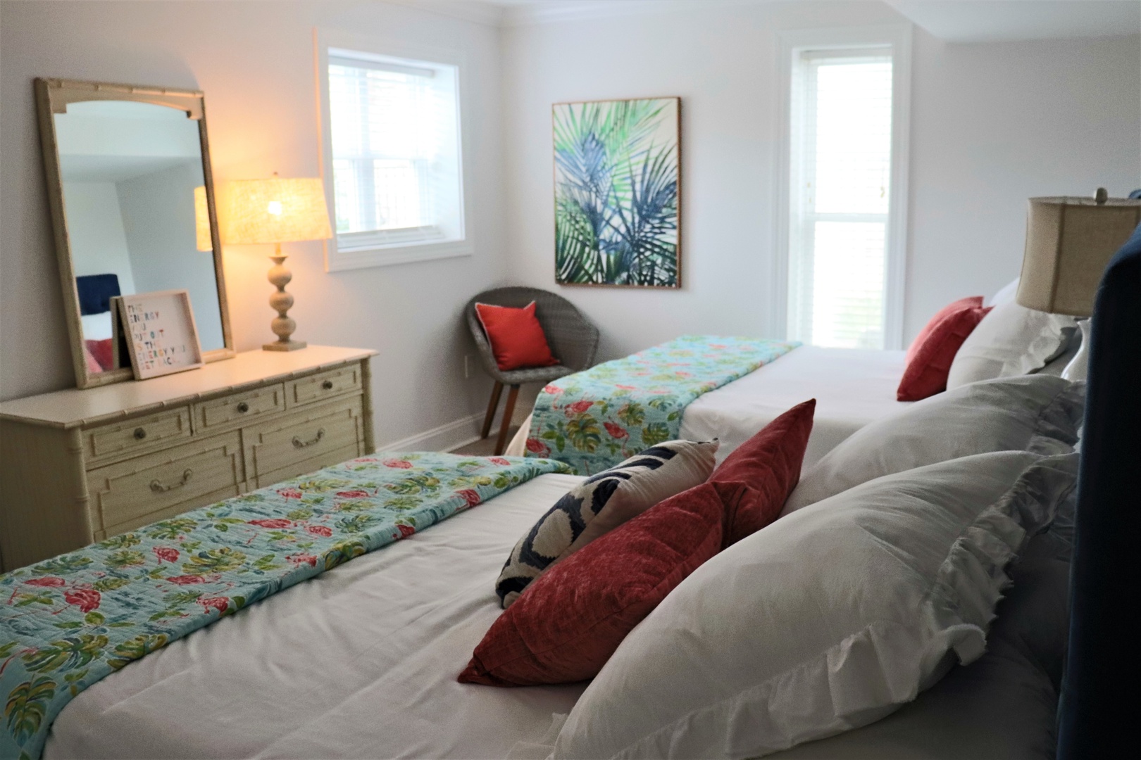 Unwind in this bright bedroom with twin beds, tropical touches, and natural light streaming through windows.