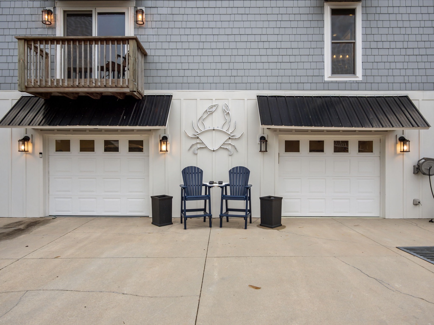 Coastal-themed property entrance featuring charming garage doors, decorative crab artwork, and welcoming blue Adirondack chairs for a perfect beachside arrival experience.