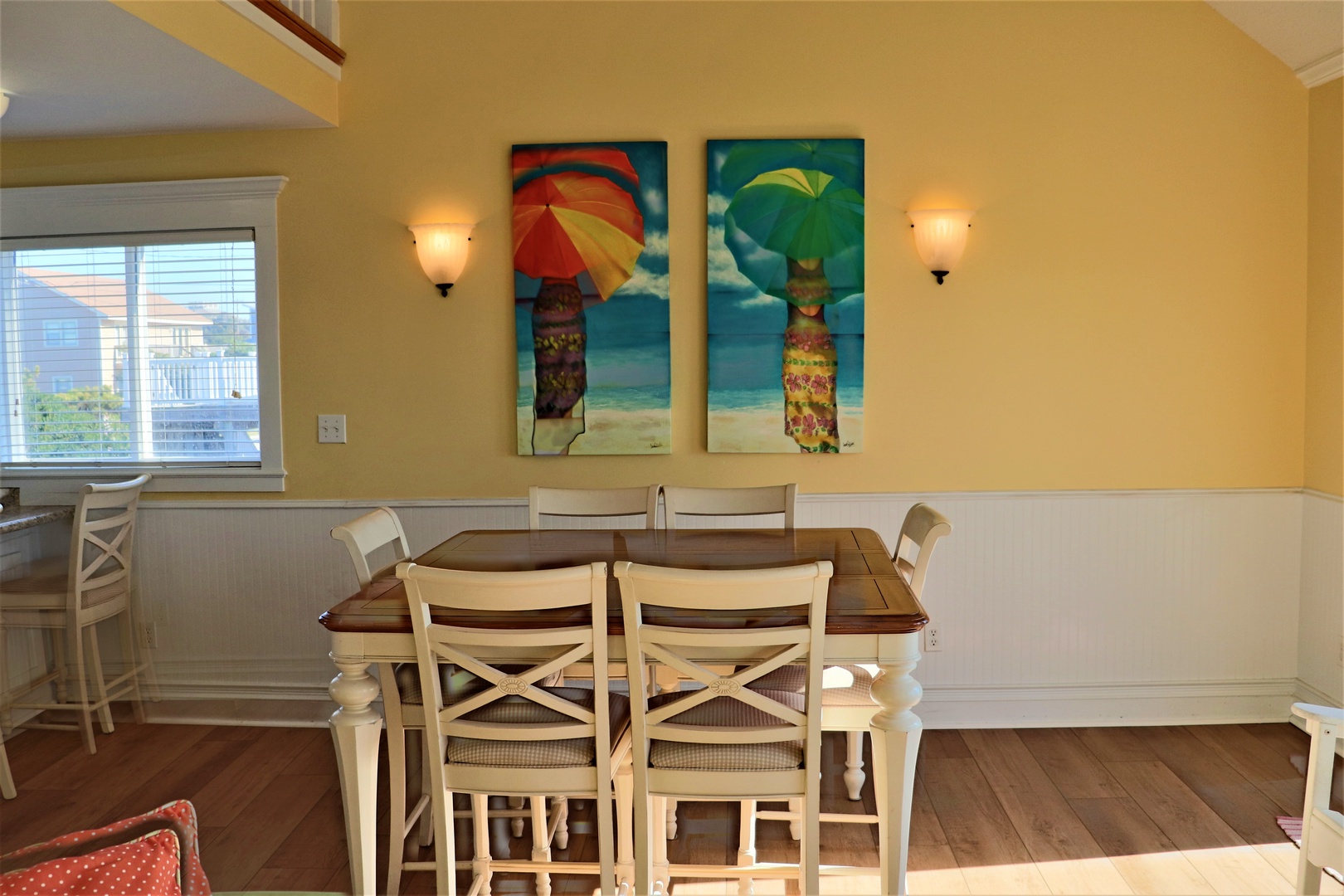 Gather around your cheerful dining table, where warm coastal artwork and soft lighting create the perfect atmosphere for memorable meals together.