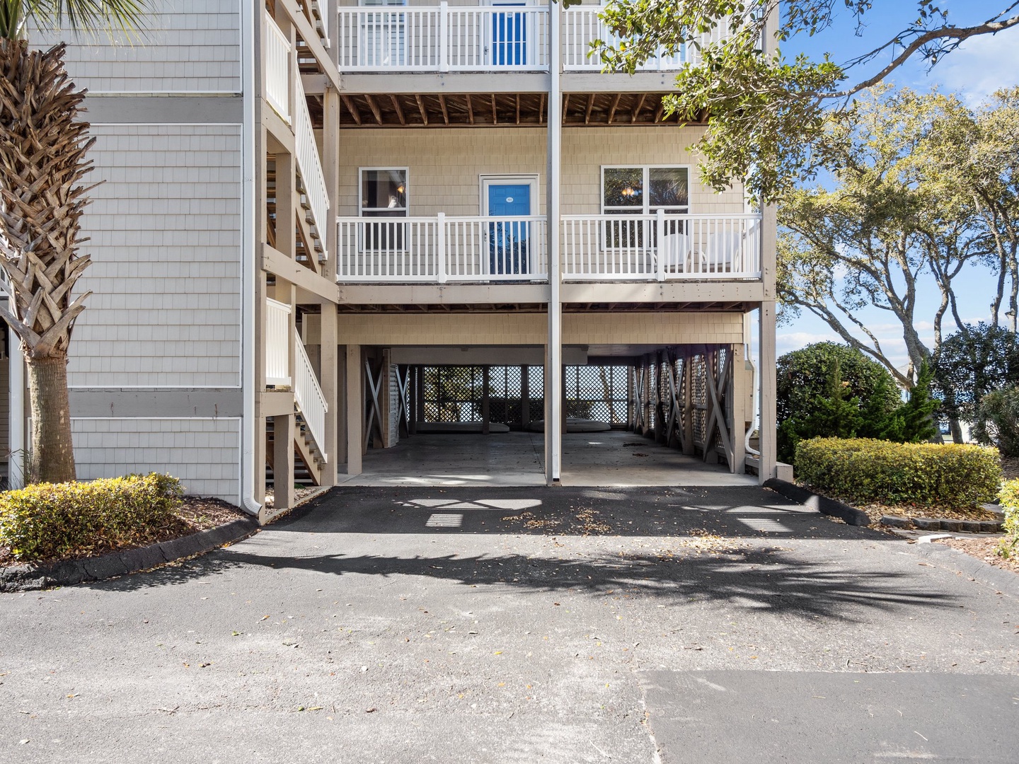 Multi-level coastal property with covered parking and balconies surrounded by mature palm trees and landscaped grounds.