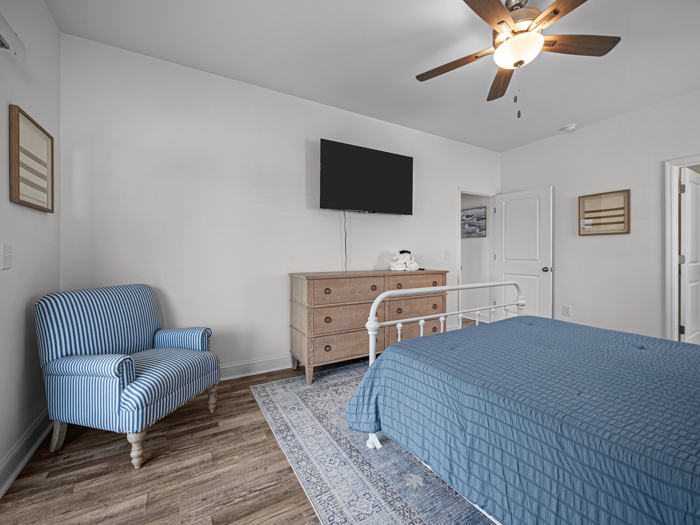 Relax in your charming bedroom with coastal blues, a cozy reading chair, and ceiling fan for perfect comfort.