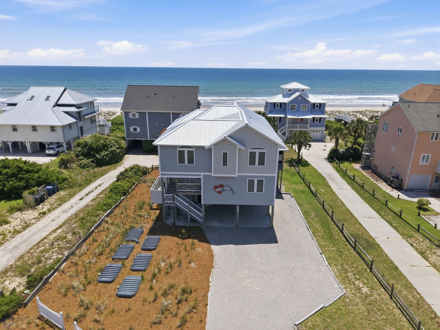 Elevated beachfront property offering direct beach access via a short path, with neighboring coastal homes and panoramic ocean views in a tranquil seaside community.