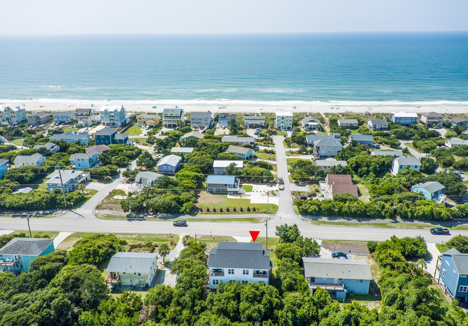 Aerial view of a beachfront vacation rental community with white sand beach and coastal homes surrounded by lush greenery.