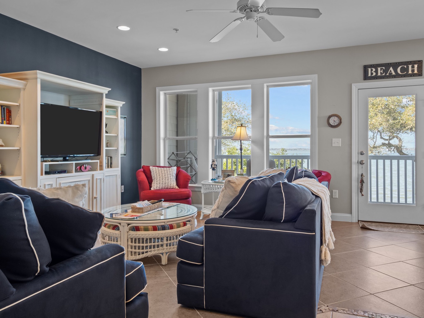 Unwind in your bright, coastal-themed living space with navy furnishings, built-in entertainment center, and peaceful water views through large windows.