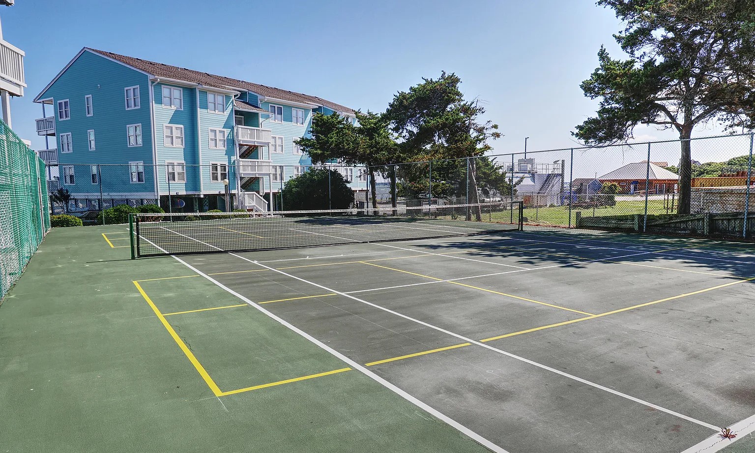 Well-maintained tennis court surrounded by coastal residential buildings, offering recreational activities during your stay.
