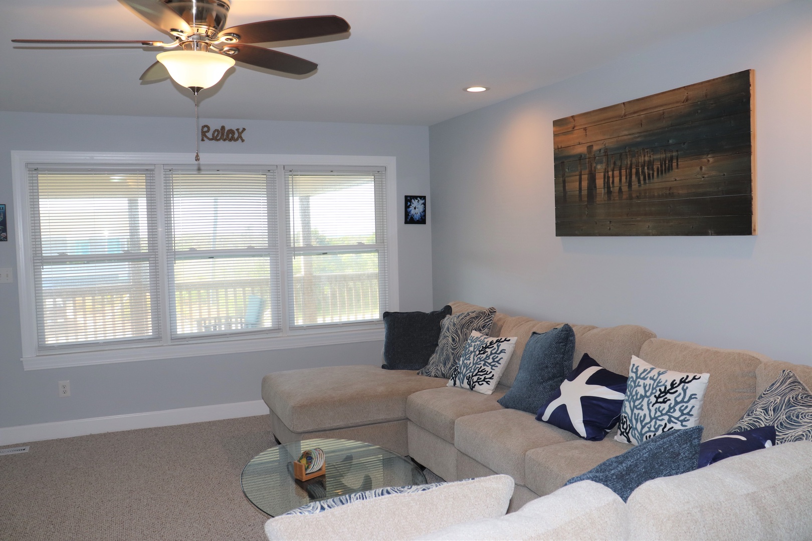 Sink into this plush sectional with coastal-themed pillows, where you can unwind under the gentle ceiling fan's breeze while enjoying natural light from the large windows.