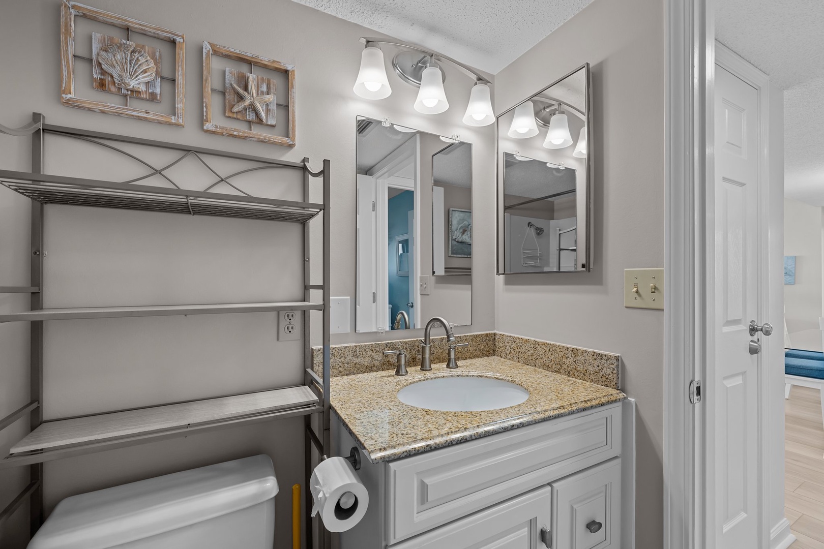 Freshen up in your coastal-themed bathroom with granite countertops, beach artwork, and bright vanity lighting.