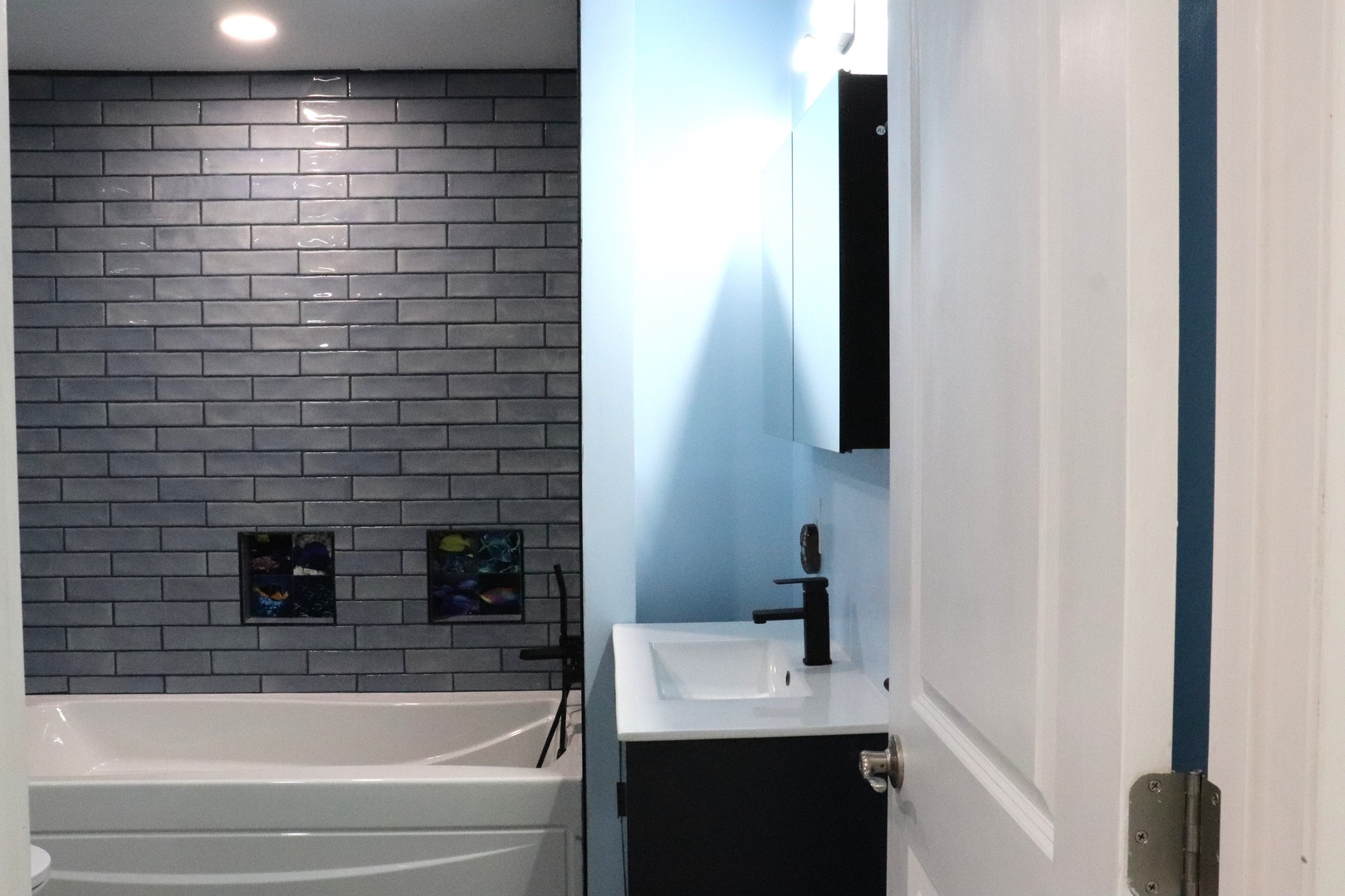 Step into your private bathroom featuring a sleek soaking tub framed by modern subway tile. Clean lines, matte black fixtures, and crisp finishes create a fresh, contemporary retreat.
