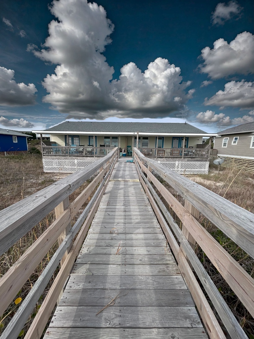 Charming beachfront property with private boardwalk leading to elevated deck and wraparound porch overlooking coastal scenery.