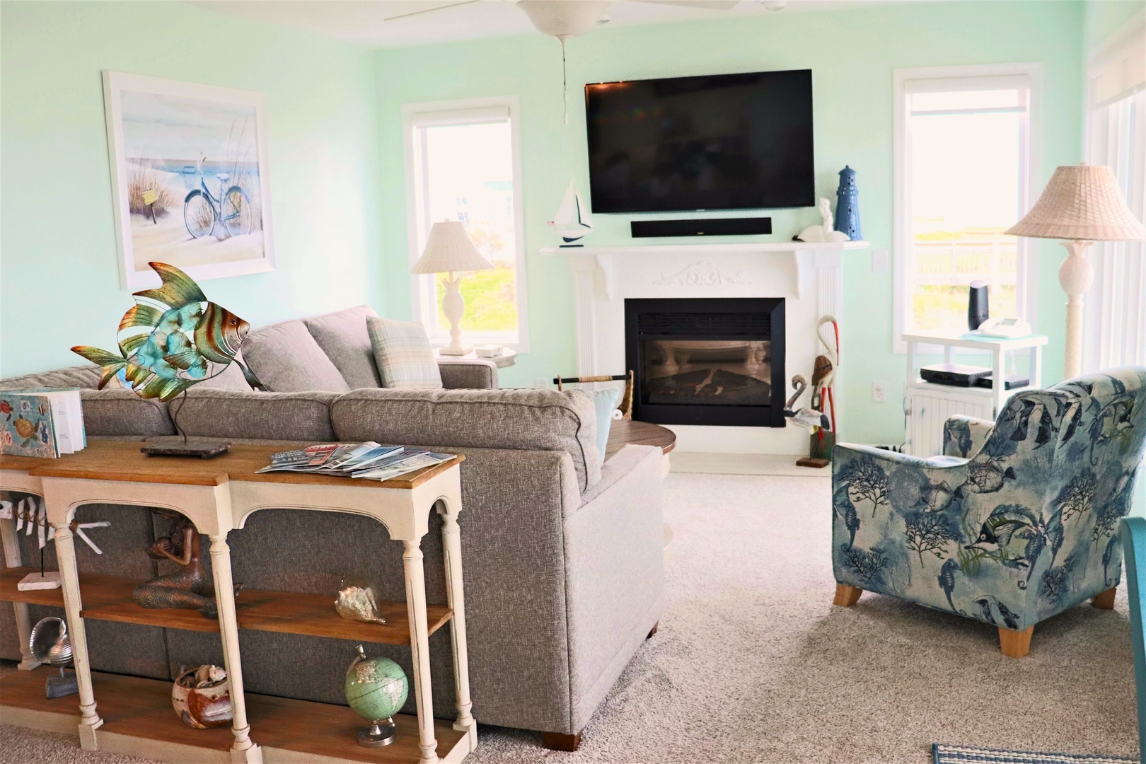 Settle into your bright, coastal-themed living room where soft mint walls and comfortable seating create the perfect spot for movie nights by the cozy fireplace.
