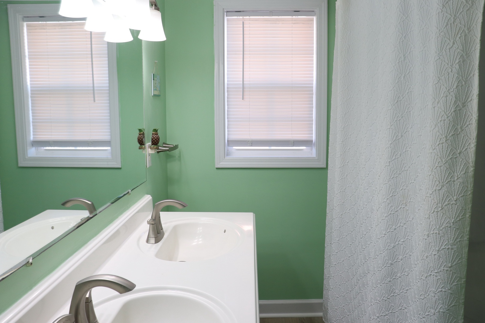 Refresh in this bright bathroom featuring soothing green walls, dual sinks, and natural light streaming through privacy blinds.