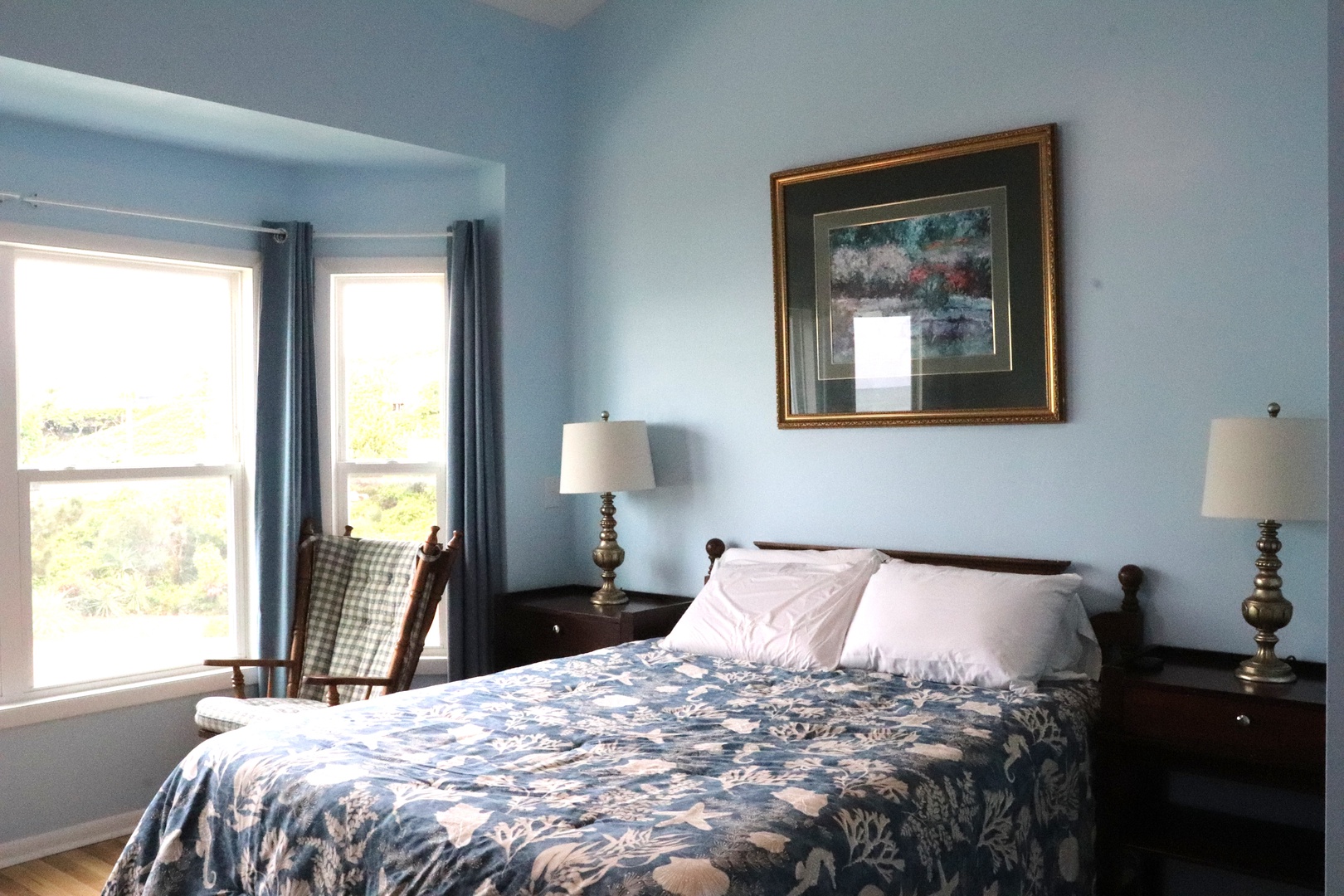 You'll love unwinding in this peaceful bedroom with its calming blue walls, plush bedding, and abundant natural light streaming through double windows overlooking the greenery outside.