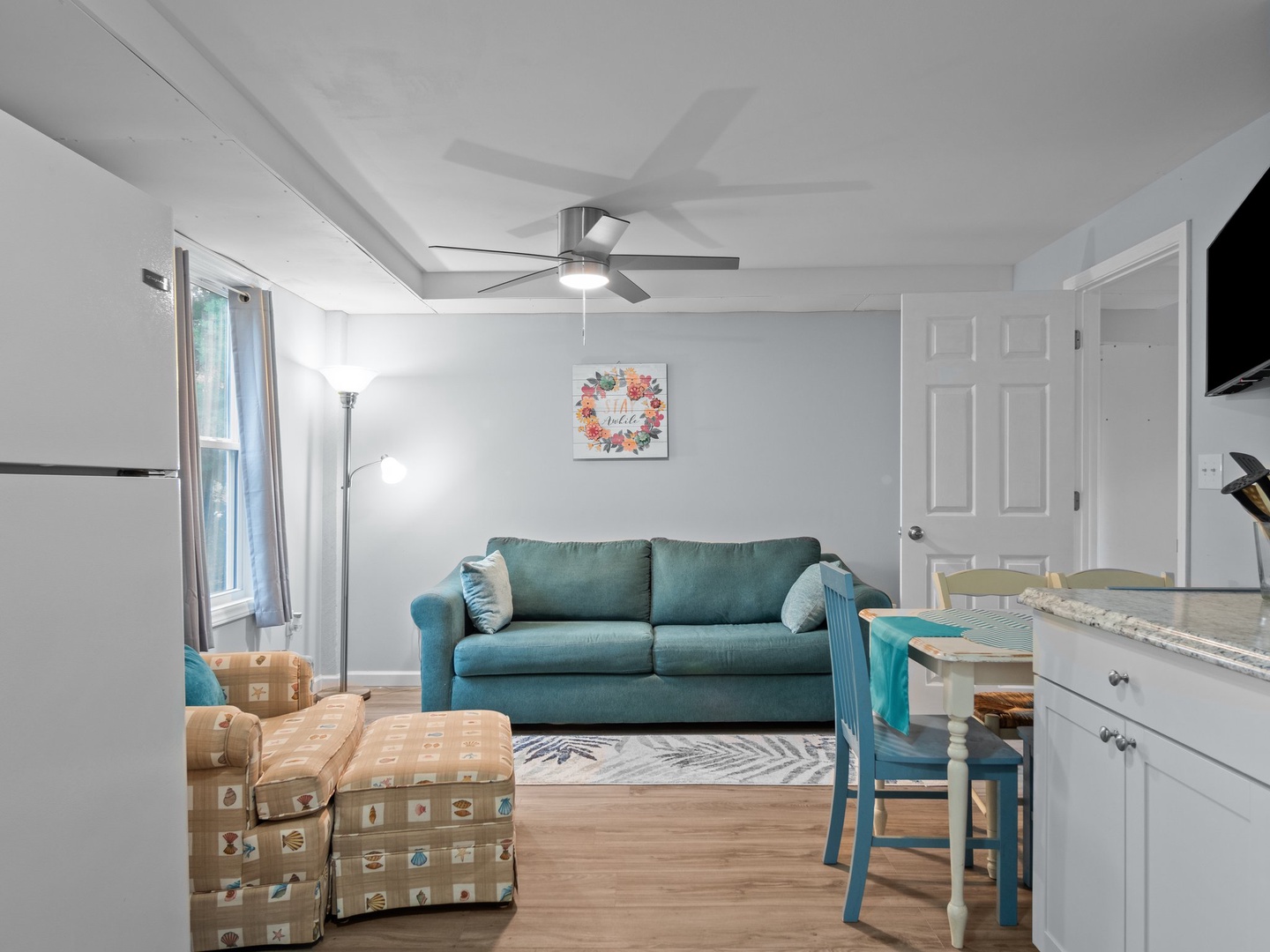 Step into your bright, coastal-inspired living space with teal sofa, exposed beams overhead, and kitchen nearby for easy meal prep.