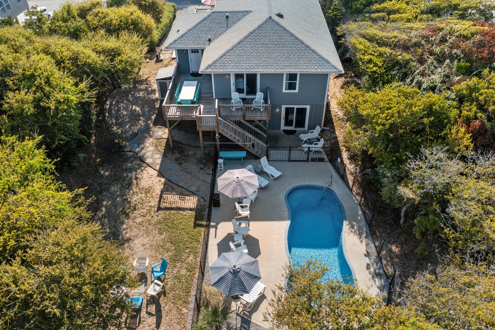 Aerial view of charming coastal home with private pool, multi-level decks, and lush tree-lined setting for peaceful getaway.