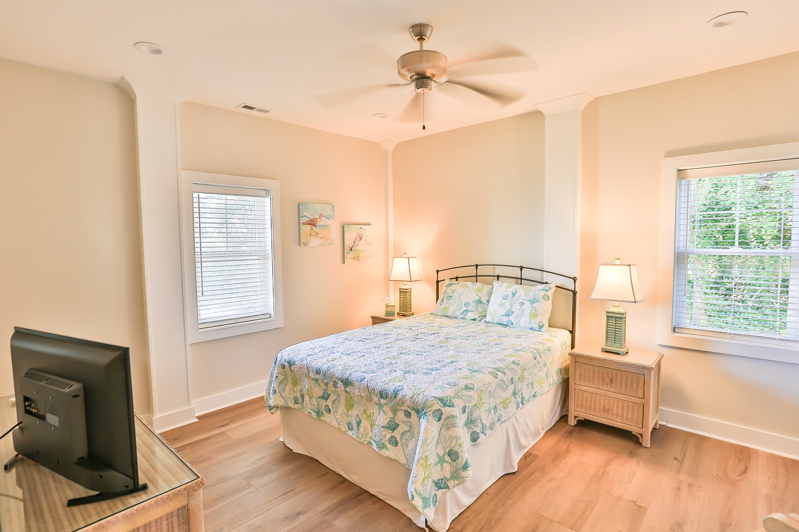 Drift into peaceful sleep in your bright bedroom with tropical bedding, ceiling fan, and windows overlooking lush greenery.