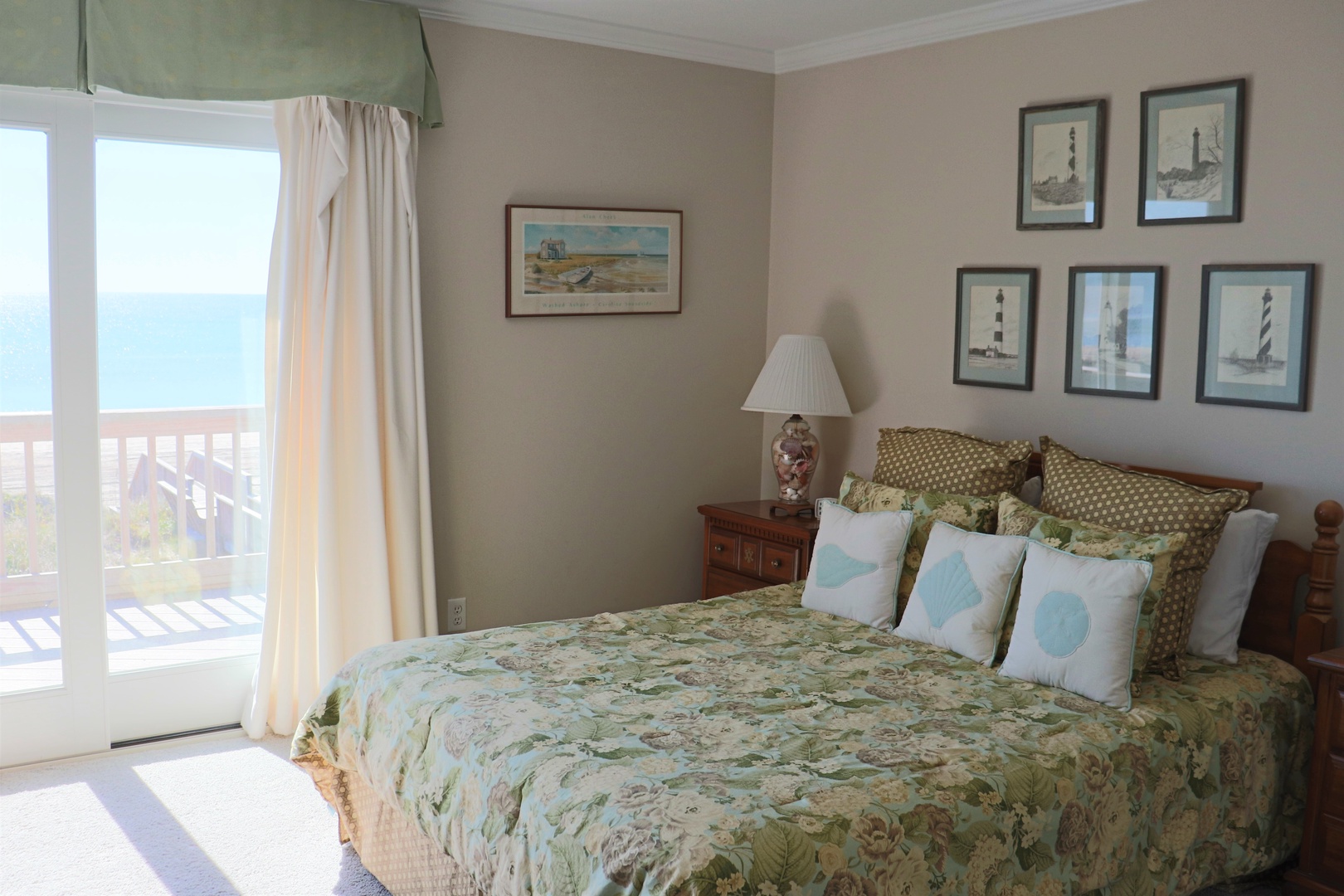 Your coastal-themed bedroom opens to ocean views, with charming nautical artwork and serene green linens creating a peaceful seaside retreat.