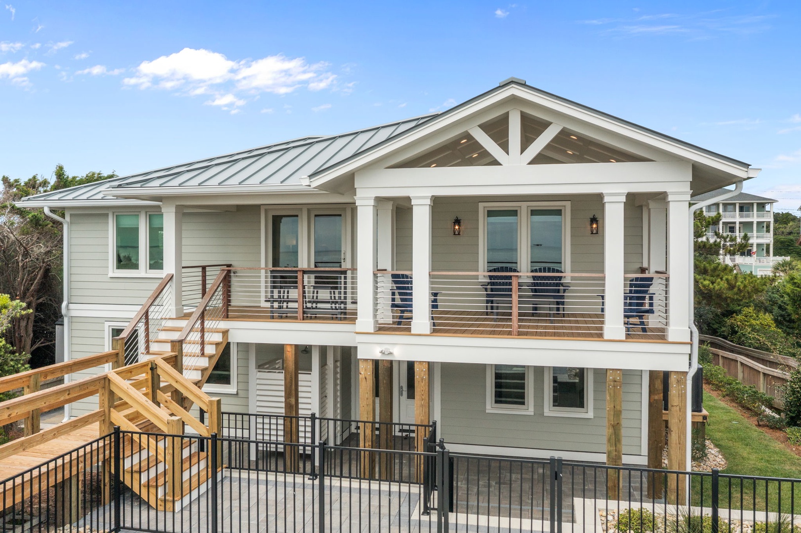 Modern coastal home featuring spacious covered porches and metal roofing, nestled among mature trees in a peaceful residential setting.