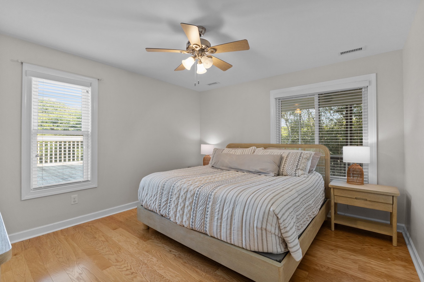 Drift off in this peaceful bedroom featuring a comfortable queen bed, gentle ceiling fan breeze, and natural light from dual windows.