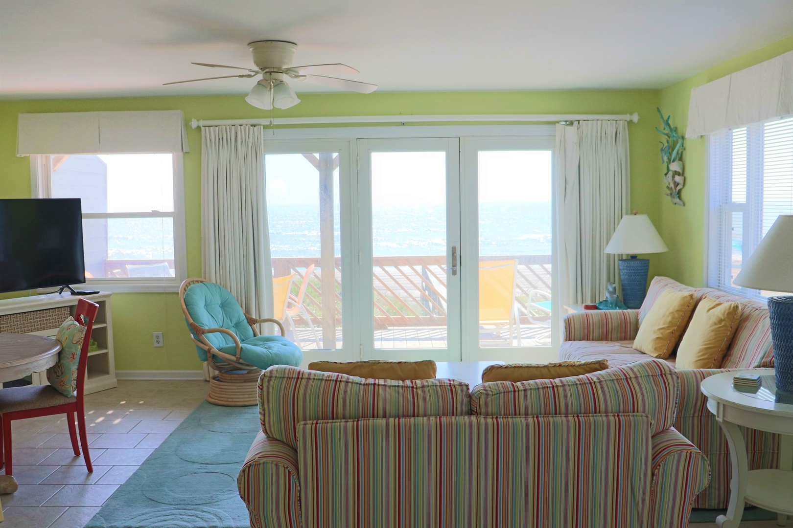 Your bright, tropical living room opens to stunning ocean views through sliding doors, perfect for relaxing on colorful furniture while sea breezes flow through.