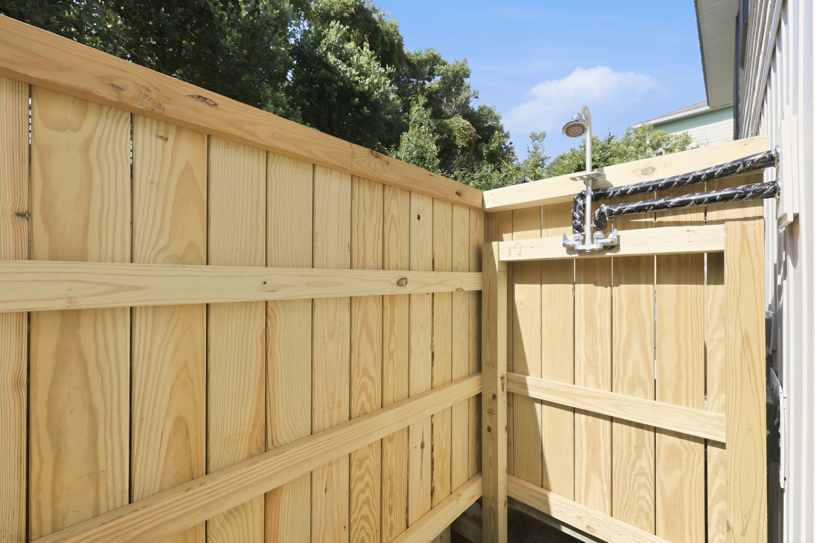 A private outdoor shower enclosed by fresh wooden fencing, where you can rinse off after a day at the beach or pool in total seclusion.
